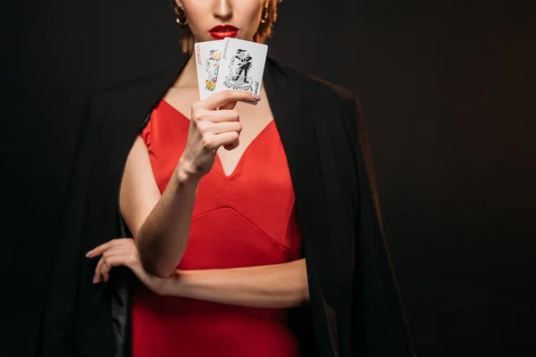 Imagem cortada de menina em vestido vermelho e jaqueta preta segurando cartões de poker isolados em preto — Fotografia de Stock