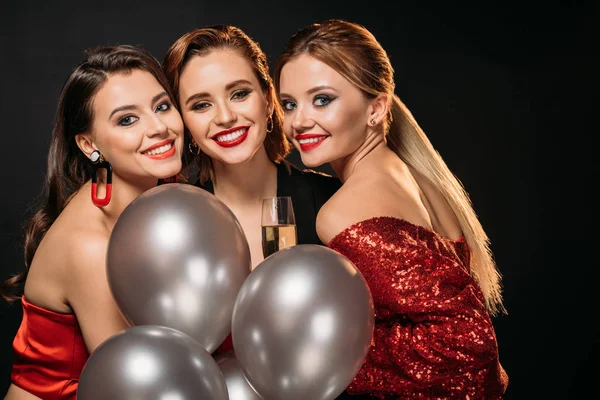 Портрет улыбающихся привлекательных девушек в стильной одежде для вечеринок, держащих связку серых воздушных шаров, изолированных на черном — стоковое фото