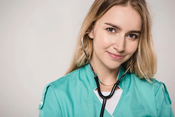 Attractive female doctor with stethoscope in ears  isolated on grey — Stock Photo