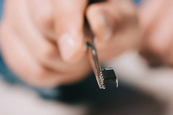 Foco seletivo de pinças com microchip na mão do homem — Fotografia de Stock