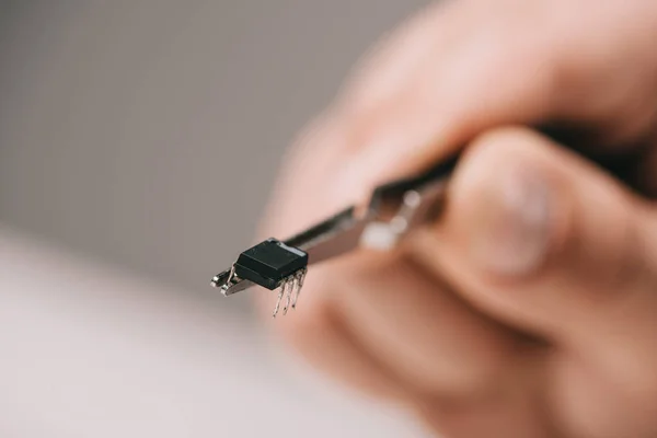 Cropped view of tweezers with microchip hand of man on grey background — Stock Photo