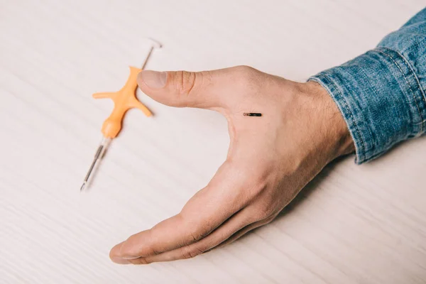 Ausgeschnittene Ansicht der männlichen Hand mit Mikrochip und Spritze zum Mikrochippen auf dem Tisch — Stockfoto