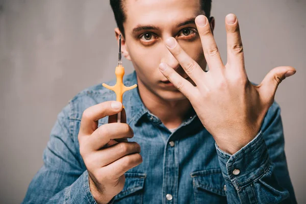 Schöner Mann zeigt Hand und hält Spritze zum Mikrochippen auf grauem Hintergrund — Stockfoto