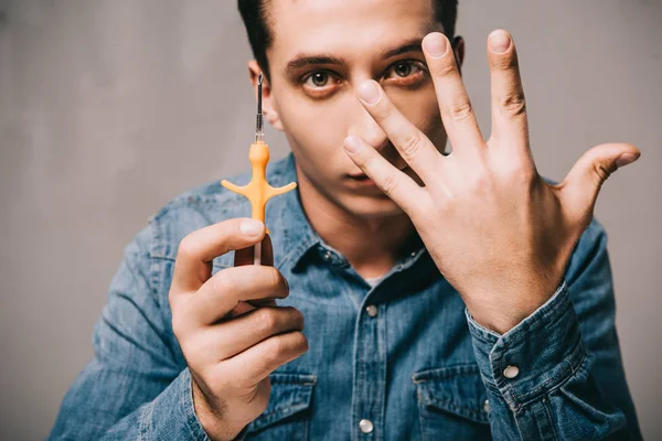 Homem bonito mostrando mão e segurando seringa para microchip em fundo cinza — Fotografia de Stock