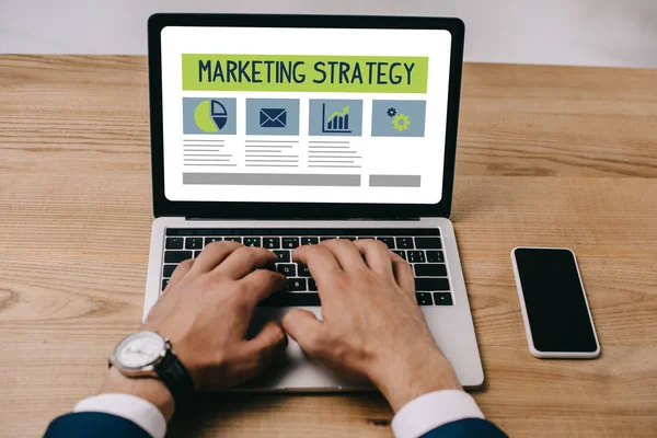 Abgeschnittene Ansicht des Geschäftsmannes, der auf Laptop mit Marketing-Strategie-Symbolen tippt — Stockfoto