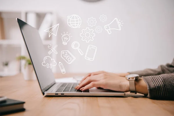 Vista cortada de empresária trabalhando e digitando no laptop com ícones seo — Fotografia de Stock