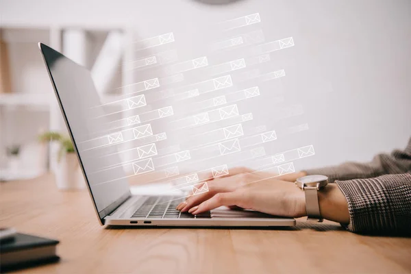 Cropped view of businesswoman working and typing on laptop with sending e-mails icons — Stock Photo