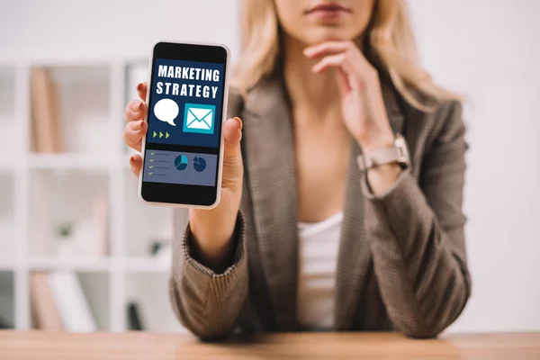 Ausgeschnittene Ansicht einer Geschäftsfrau, die Smartphone mit Marketingstrategie präsentiert — Stockfoto