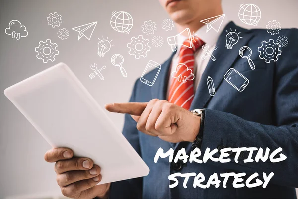 Vista recortada de hombre de negocios utilizando tableta digital con iconos de estrategia de marketing - foto de stock