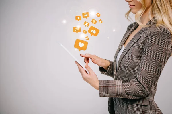 Ausgeschnittene Ansicht einer Geschäftsfrau im Anzug, die ein digitales Tablet mit Multimedia-Icons in grau berührt — Stockfoto