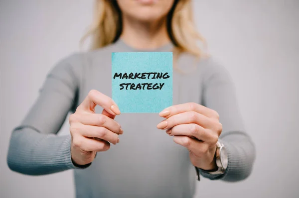 Vista cortada da mulher segurando nota de papel azul com estratégia de marketing isolado em cinza — Fotografia de Stock