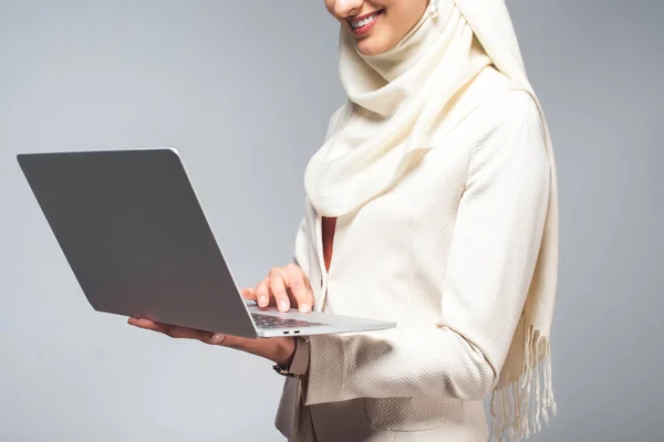 Cropped shot of smiling young muslim woman using laptop isolated on grey — Stock Photo