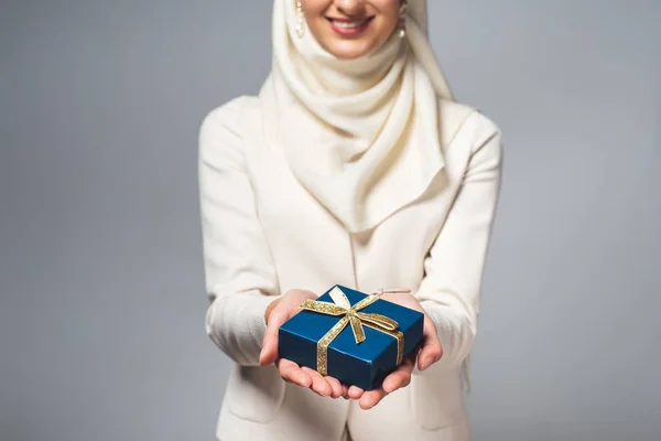 Ritagliato colpo di sorridente giovane donna musulmana in possesso di scatola regalo isolato su grigio — Foto stock