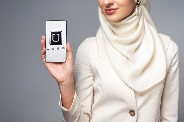 Cropped shot of smiling muslim woman holding smartphone with uber app isolated on grey — Stock Photo