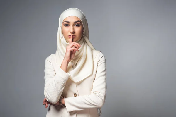 Young muslim woman standing with finger on lips and looking at camera isolated on grey — Stock Photo