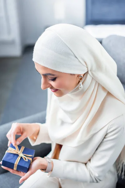 Улыбающаяся молодая мусульманка открывает подарочную коробку дома — стоковое фото