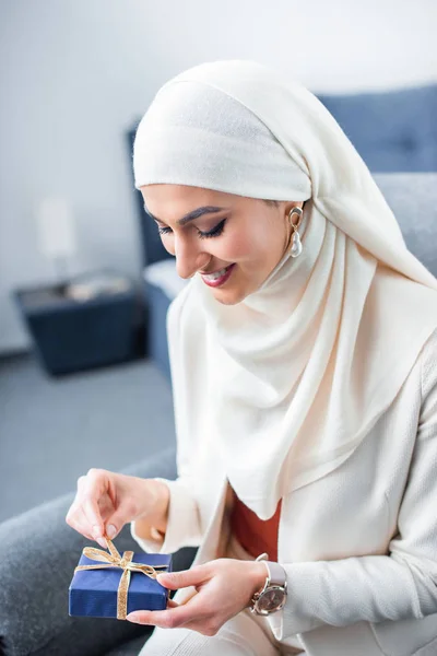 Felice giovane donna musulmana apertura confezione regalo a casa — Foto stock