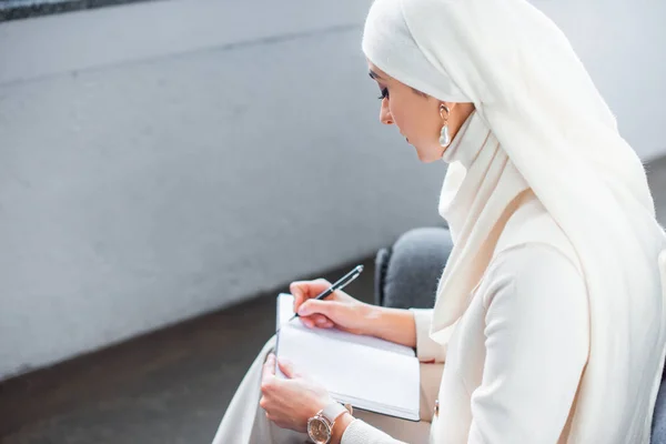 Visão de alto ângulo da jovem mulher muçulmana escrevendo em notebook em casa — Fotografia de Stock