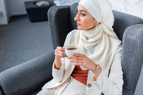 Young muslim woman holding cup of coffee and looking away at home — Stock Photo