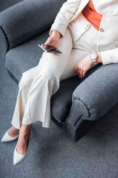 Cropped shot of young woman sitting in armchair and using smartphone — Stock Photo