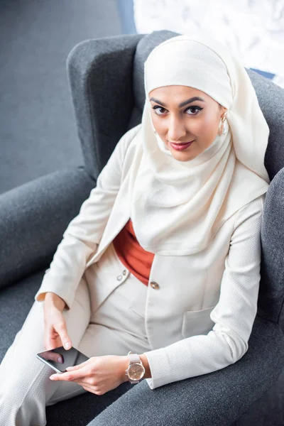 High angle view of young muslim woman using smartphone and smiling at camera — Stock Photo