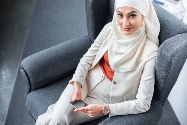 High angle view of beautiful muslim woman using smartphone and smiling at camera — Stock Photo