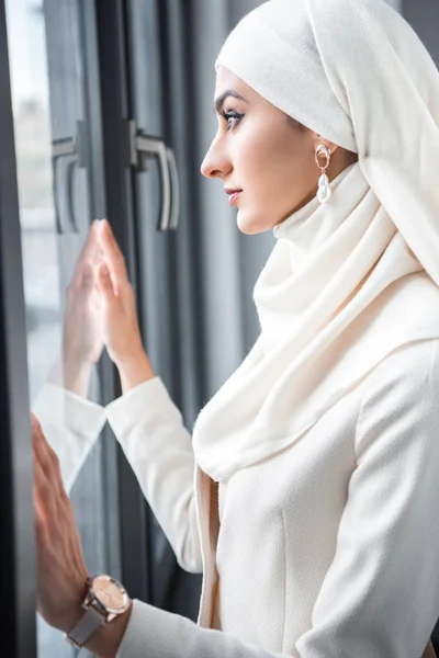Vista lateral de la joven musulmana mirando a la ventana - foto de stock