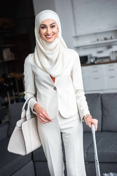 Beautiful young muslim woman holding suitcase and smiling at camera — Stock Photo