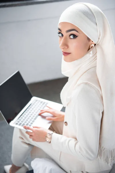 Привлекательная мусульманка использует ноутбук с чистым экраном и смотрит в камеру — стоковое фото