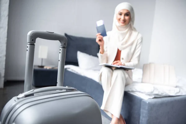 Close-up vista da mala e mulher muçulmana sorridente segurando passaporte com cartão de embarque em casa — Fotografia de Stock