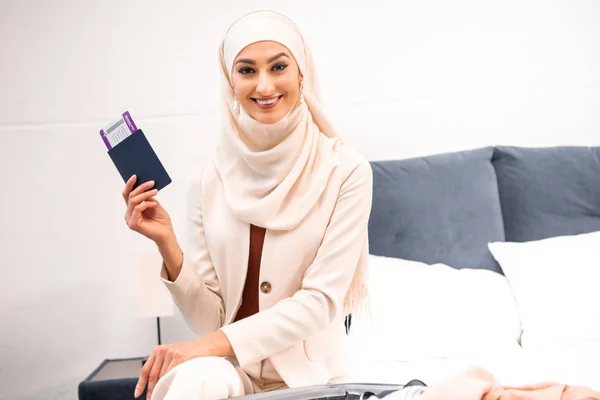 Heureuse jeune femme musulmane tenant passeport avec carte d'embarquement et souriant à la caméra — Photo de stock