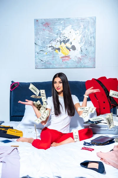 Jolie fille brune assise sur le lit et jetant des billets en dollars — Photo de stock
