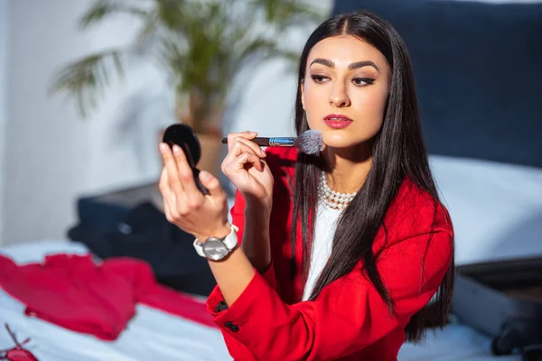 Attractive brunette girl applying makeup and looking at small mirror — Stock Photo