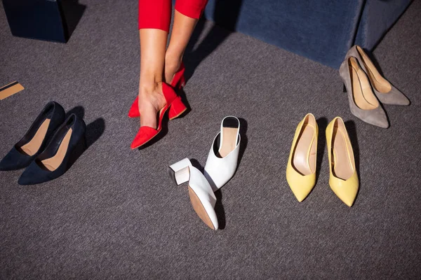 Sección baja de chica en zapatos rojos con estilo y varios calzado de moda en la alfombra - foto de stock