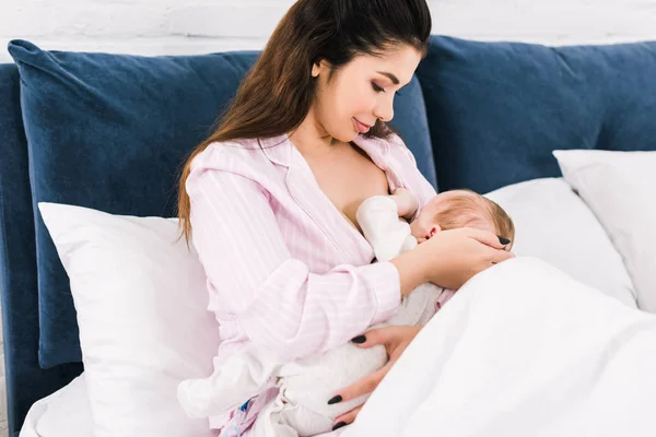 Porträt einer jungen Mutter, die ihr kleines Baby zu Hause im Bett stillt — Stockfoto