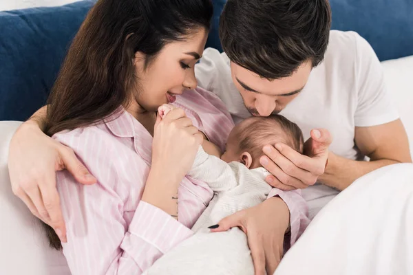 Young mother breastfeeding little baby with husband near by on bed at home — Stock Photo