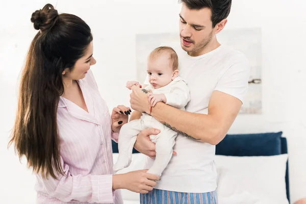 Lächelnde Mutter, die ihren kleinen Sohn zu Hause auf die Hände des Vaters schaut — Stockfoto