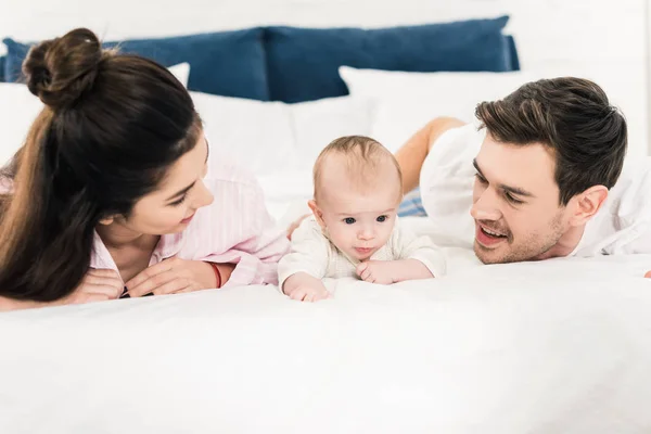 Retrato de los padres jóvenes y el pequeño bebé acostados en la cama juntos en casa - foto de stock