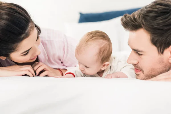 Retrato de los padres jóvenes y el pequeño bebé acostados en la cama juntos en casa - foto de stock