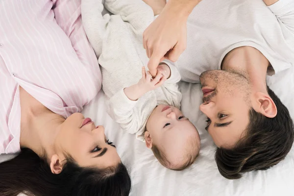 Vista aérea de la familia feliz con el pequeño bebé acostado en la cama juntos - foto de stock