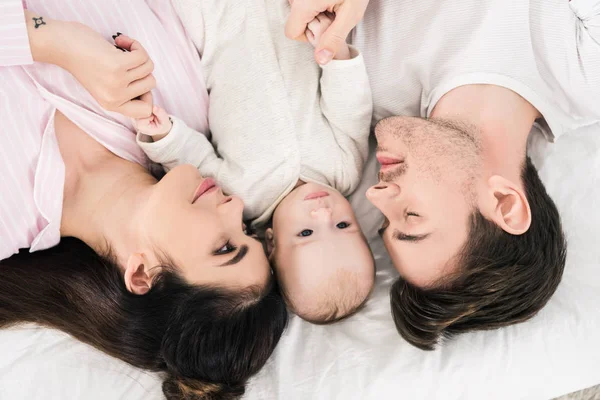 Vue aérienne de la famille heureuse avec un petit bébé couché sur le lit ensemble — Photo de stock