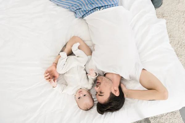 Над головой вид молодого отца и малыша лежащих на кровати вместе дома — стоковое фото