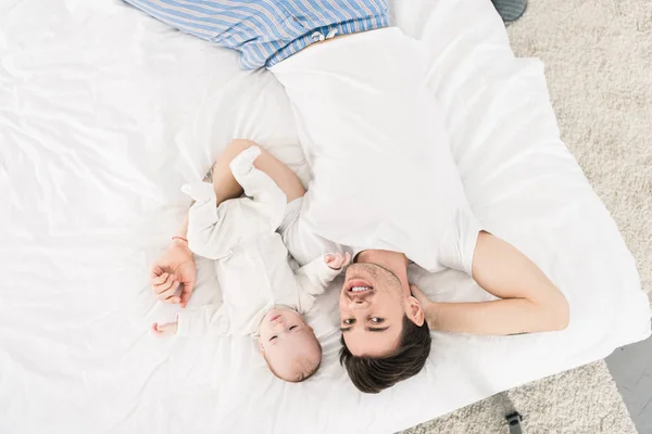 Overhead view of young father and little baby lying on bed together at home — Stock Photo