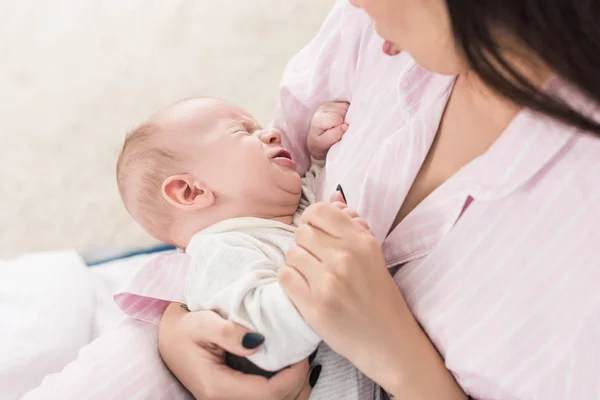 Vue partielle de la mère apaisant petit bébé pleurant sur les mains — Photo de stock