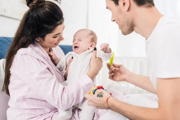 Mãe segurando choro bebê em mãos com o pai por perto em casa — Fotografia de Stock