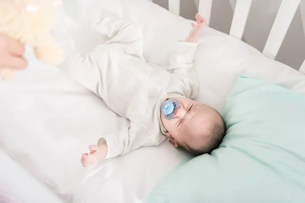 Partial view of parent showing toy to crying baby in crib — Stock Photo