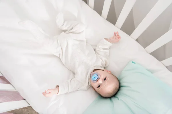 Overhead view of little baby with pacifier lying in crib — Stock Photo