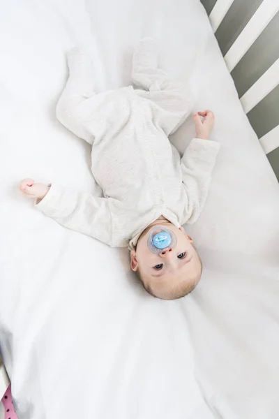 Overhead view of little baby with pacifier lying in crib — Stock Photo