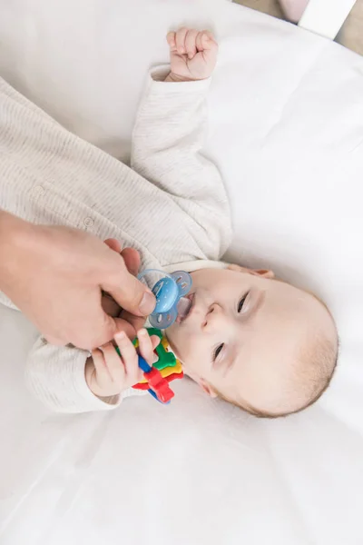 Tiro cortado de pai dando chupeta ao pequeno filho no berço — Fotografia de Stock