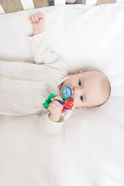 Overhead view of little baby with pacifier holding toy while lying in crib — Stock Photo